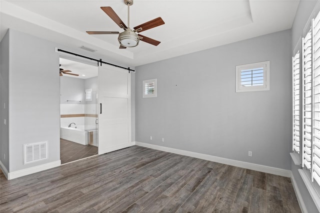 empty room with a tray ceiling, visible vents, a barn door, and a wealth of natural light