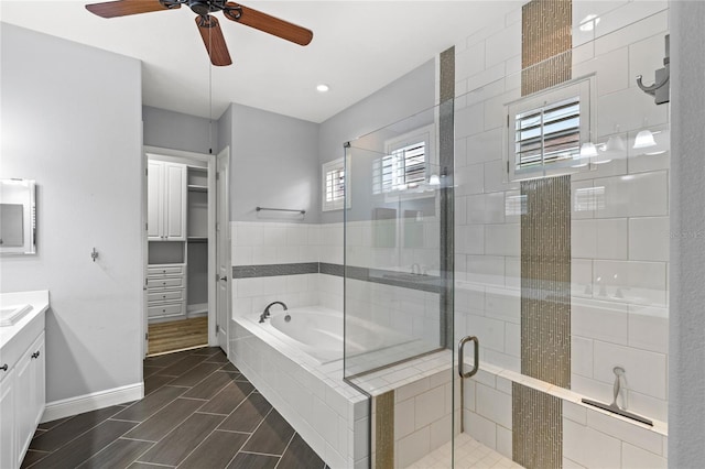 full bathroom with vanity, baseboards, a stall shower, a walk in closet, and a garden tub