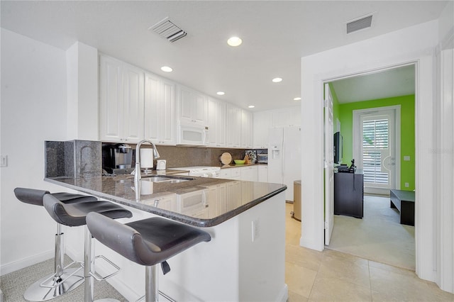 kitchen featuring a kitchen bar, white appliances, kitchen peninsula, and sink