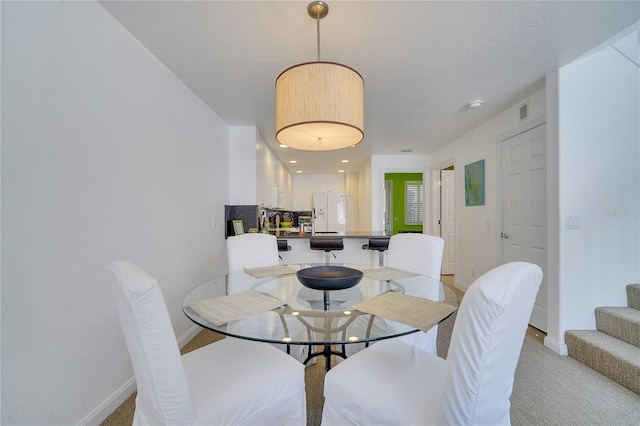 carpeted dining area with a textured ceiling