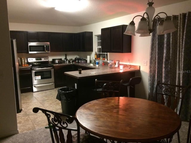 kitchen with a notable chandelier, stainless steel appliances, kitchen peninsula, and light tile patterned flooring