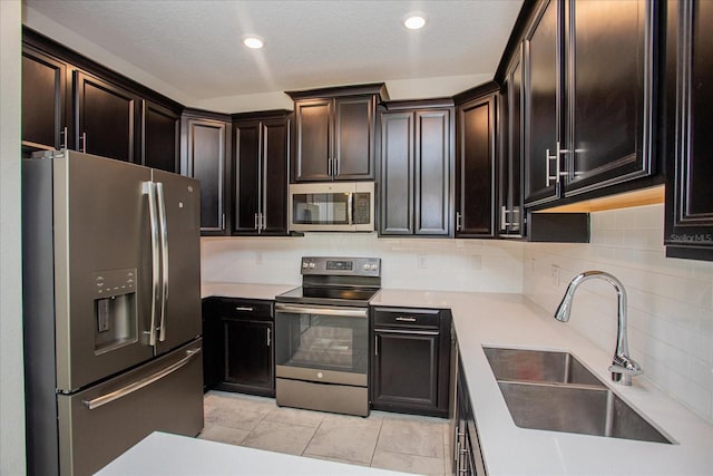 kitchen with tasteful backsplash, dark brown cabinets, appliances with stainless steel finishes, light tile patterned floors, and sink