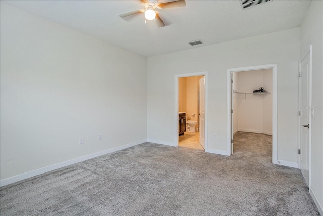 unfurnished bedroom featuring ceiling fan, ensuite bathroom, light carpet, a walk in closet, and a closet