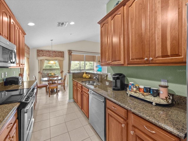 kitchen featuring lofted ceiling, appliances with stainless steel finishes, dark stone countertops, light tile patterned flooring, and sink