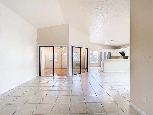 spare room with a textured ceiling, ceiling fan, light tile patterned flooring, and vaulted ceiling