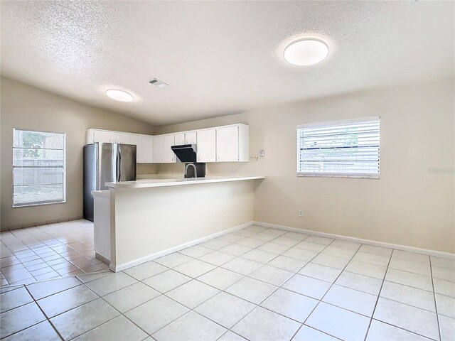 kitchen featuring kitchen peninsula, a textured ceiling, white cabinets, lofted ceiling, and light tile patterned flooring