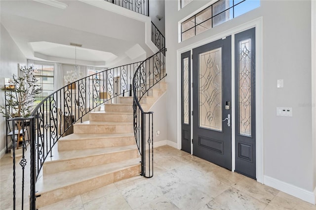 tiled foyer entrance featuring a towering ceiling, a raised ceiling, and an inviting chandelier