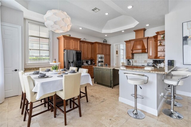 kitchen featuring light tile patterned floors, stainless steel fridge with ice dispenser, custom exhaust hood, backsplash, and a raised ceiling