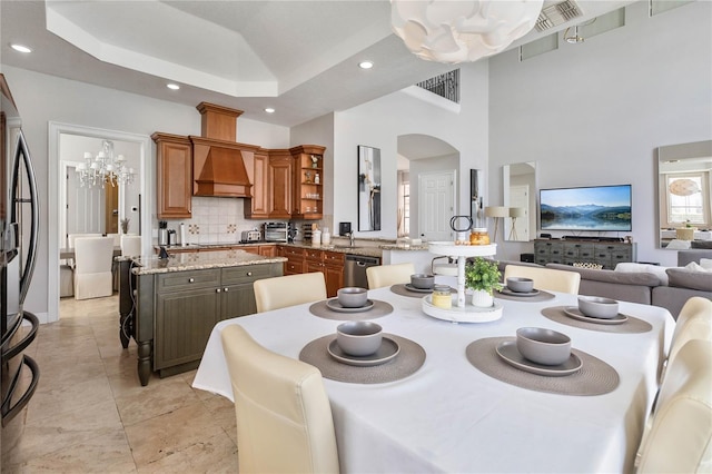 dining area featuring light tile patterned flooring, a raised ceiling, an inviting chandelier, and a towering ceiling