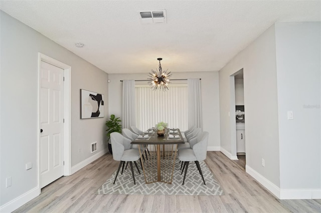 dining area with a textured ceiling, a chandelier, and light hardwood / wood-style floors