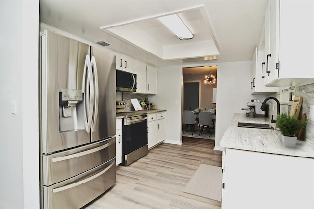 kitchen with appliances with stainless steel finishes, an inviting chandelier, sink, and white cabinets