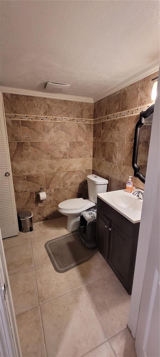 bathroom with a textured ceiling, toilet, tile walls, tile patterned flooring, and vanity