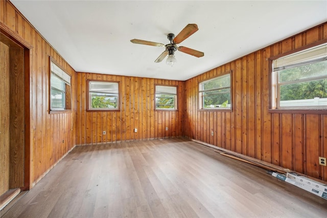 spare room with ceiling fan, plenty of natural light, wooden walls, and light wood-type flooring