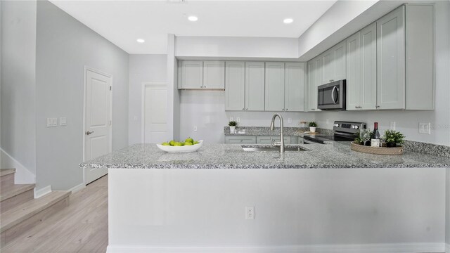 kitchen featuring appliances with stainless steel finishes, light hardwood / wood-style flooring, light stone counters, and sink