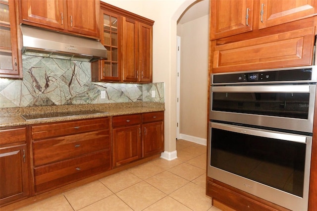 kitchen featuring stainless steel double oven, backsplash, electric cooktop, light tile patterned floors, and light stone counters