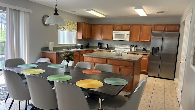 kitchen with appliances with stainless steel finishes, sink, light tile patterned floors, decorative light fixtures, and a kitchen island