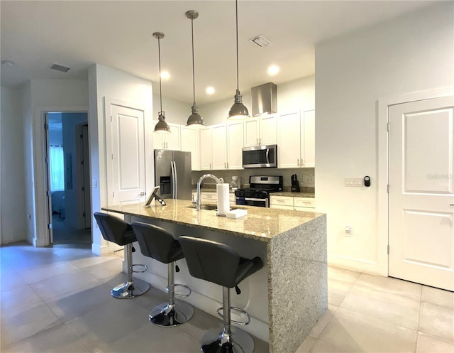 kitchen with tasteful backsplash, stainless steel appliances, an island with sink, light stone countertops, and white cabinetry