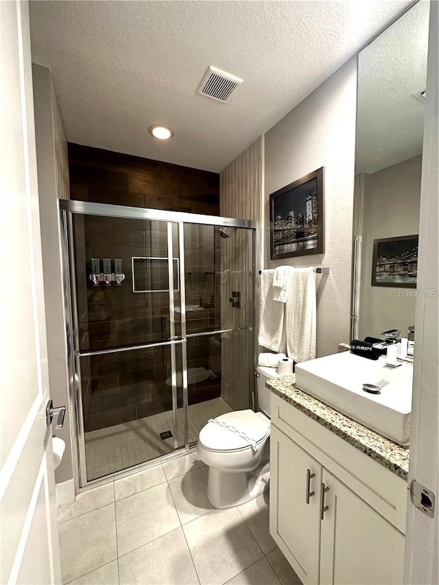 bathroom with a textured ceiling, a shower with door, toilet, tile patterned floors, and vanity