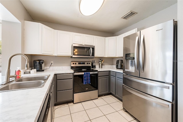 kitchen with appliances with stainless steel finishes, gray cabinetry, white cabinets, light tile patterned floors, and sink