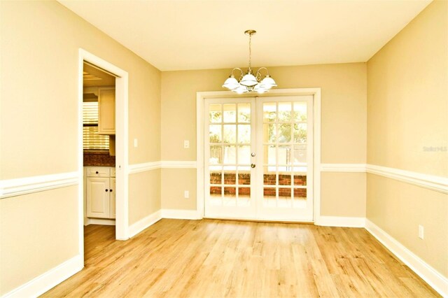 unfurnished dining area with light wood-type flooring, french doors, and an inviting chandelier