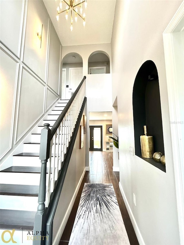 stairway featuring an inviting chandelier, hardwood / wood-style flooring, and a towering ceiling