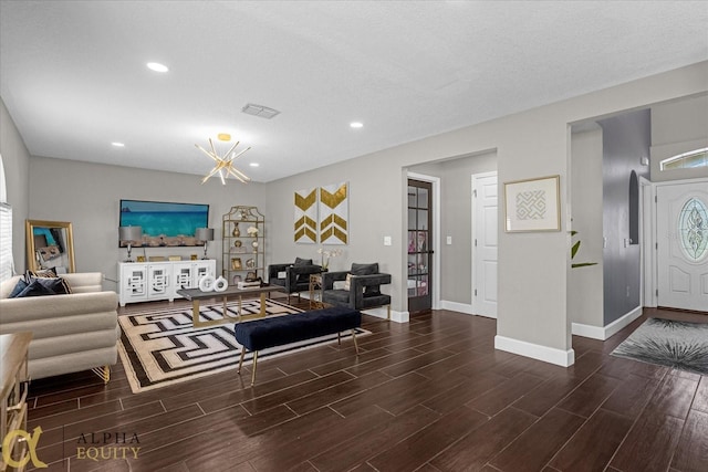 living room with a textured ceiling, a notable chandelier, and dark wood-type flooring