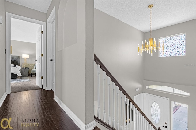 corridor with a notable chandelier, a textured ceiling, and dark carpet