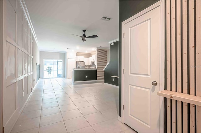 interior space featuring ceiling fan, appliances with stainless steel finishes, white cabinets, crown molding, and light tile patterned floors