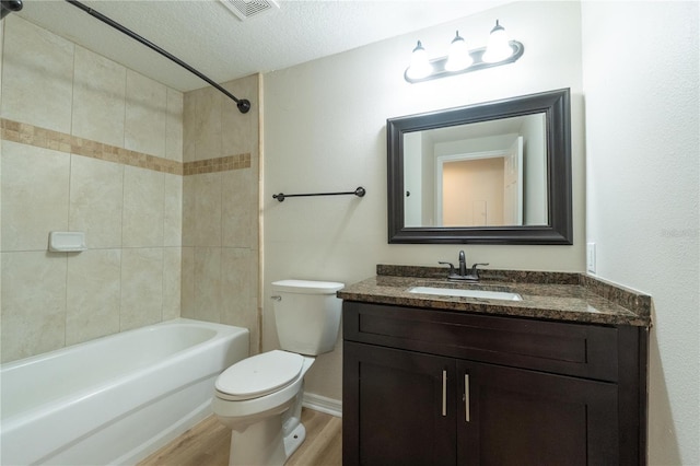 full bathroom featuring tiled shower / bath, wood-type flooring, vanity, toilet, and a textured ceiling