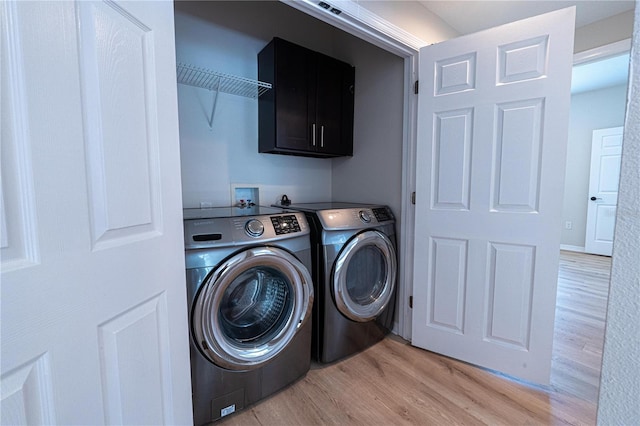 laundry area featuring cabinets, washing machine and clothes dryer, and light hardwood / wood-style floors