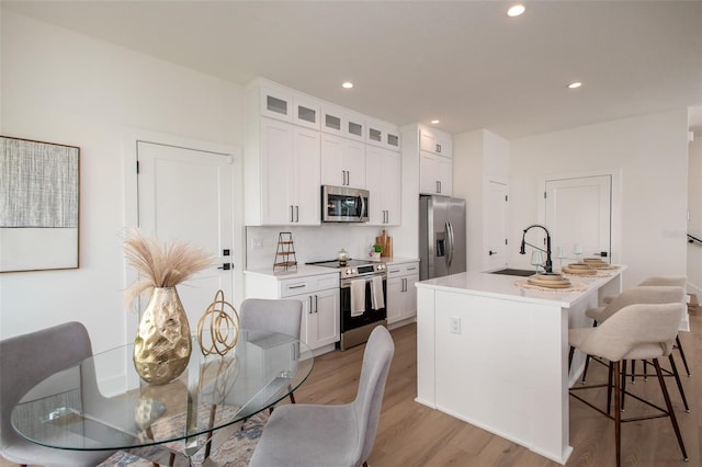 kitchen featuring white cabinets, sink, stainless steel appliances, and an island with sink