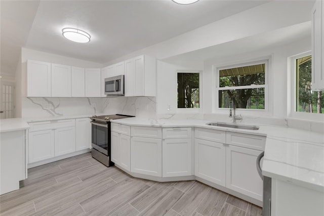 kitchen featuring white cabinetry, sink, backsplash, stainless steel appliances, and light stone countertops