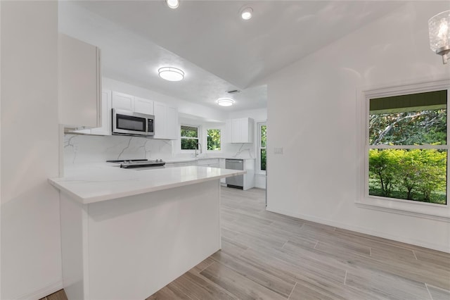 kitchen with stainless steel appliances, white cabinetry, backsplash, and kitchen peninsula