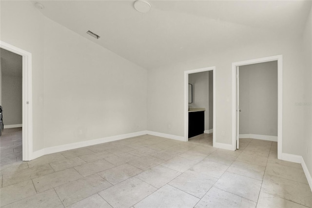 unfurnished bedroom featuring ensuite bath, light tile patterned flooring, a closet, and lofted ceiling