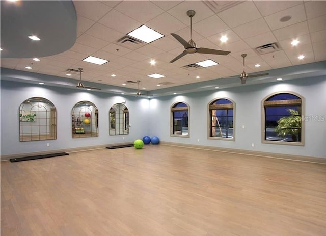 exercise room with ceiling fan, light hardwood / wood-style flooring, and a drop ceiling