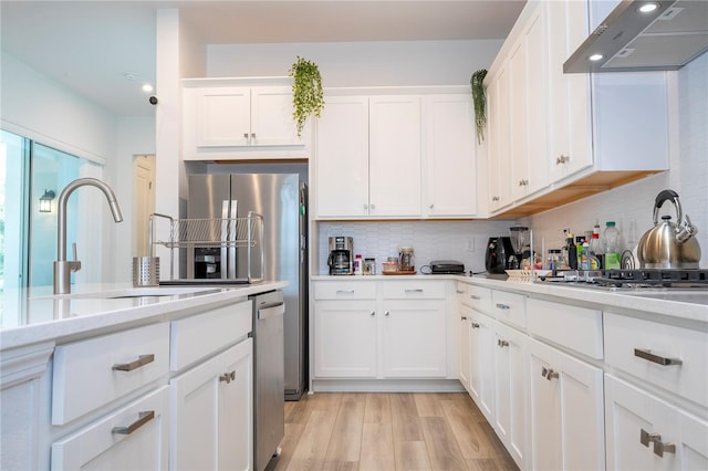 kitchen featuring light wood-type flooring, exhaust hood, sink, decorative backsplash, and white cabinets