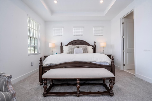 bedroom with light colored carpet and a tray ceiling