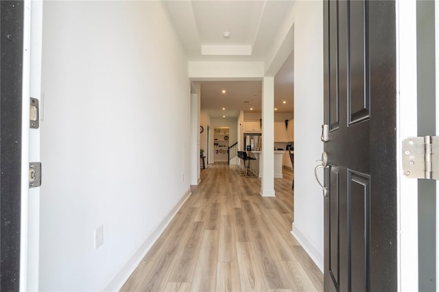 corridor featuring a tray ceiling and light hardwood / wood-style floors