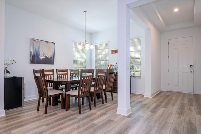 dining space featuring a raised ceiling, light wood-type flooring, and a chandelier