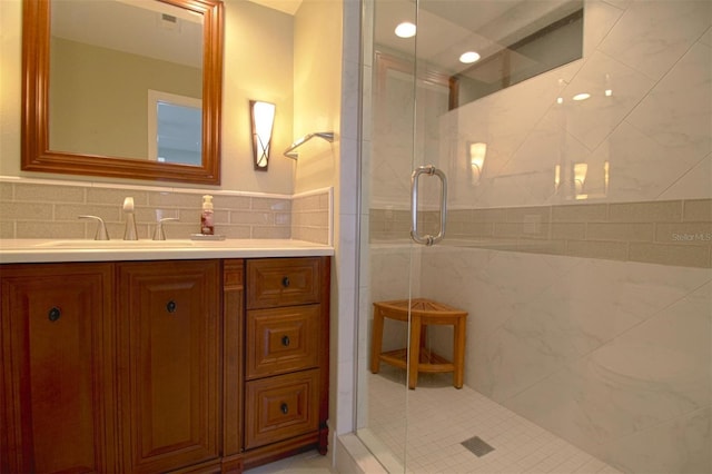 bathroom featuring vanity, a shower with shower door, tile walls, and backsplash