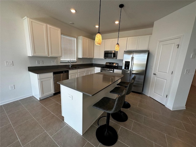 kitchen featuring stainless steel appliances, a kitchen island, sink, dark tile patterned floors, and decorative light fixtures