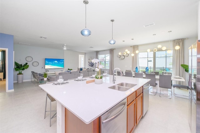 kitchen with light tile patterned floors, a kitchen island with sink, dishwasher, sink, and decorative light fixtures