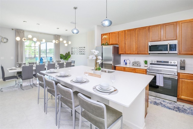 kitchen with an island with sink, appliances with stainless steel finishes, brown cabinets, light countertops, and a sink