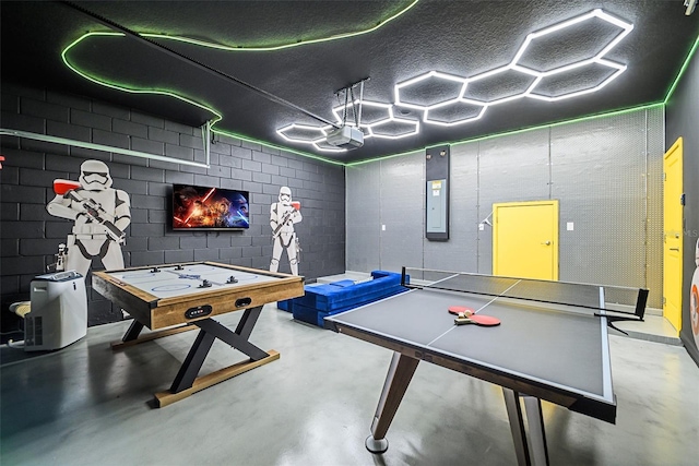 recreation room featuring finished concrete flooring, a textured ceiling, and concrete block wall