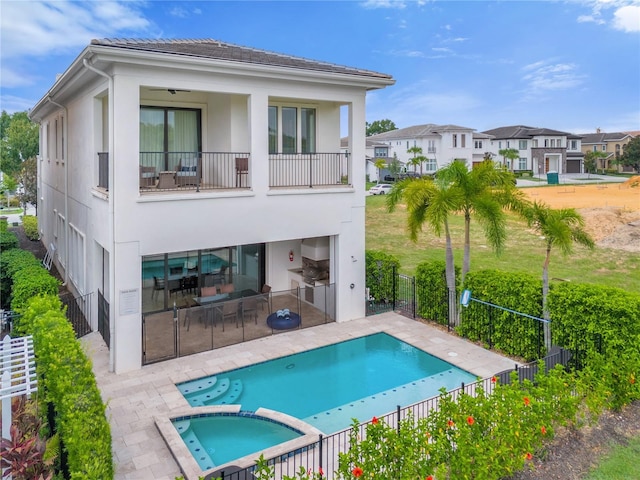 back of property featuring a balcony, a swimming pool with hot tub, exterior kitchen, and a patio