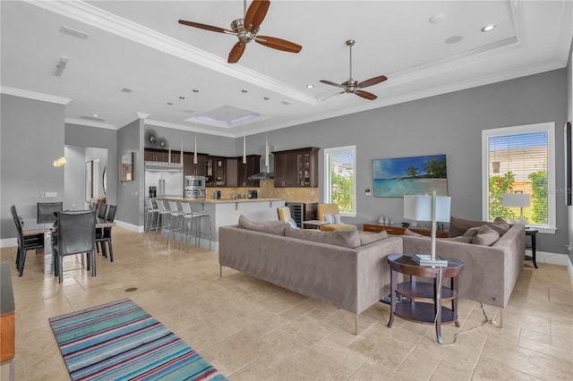 living room with a tray ceiling, light tile patterned floors, ornamental molding, and ceiling fan