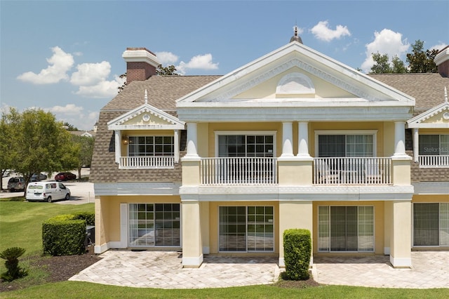 rear view of property with a balcony, a patio area, a chimney, and roof with shingles