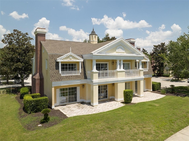 back of property with roof with shingles, a yard, a chimney, a patio, and a balcony