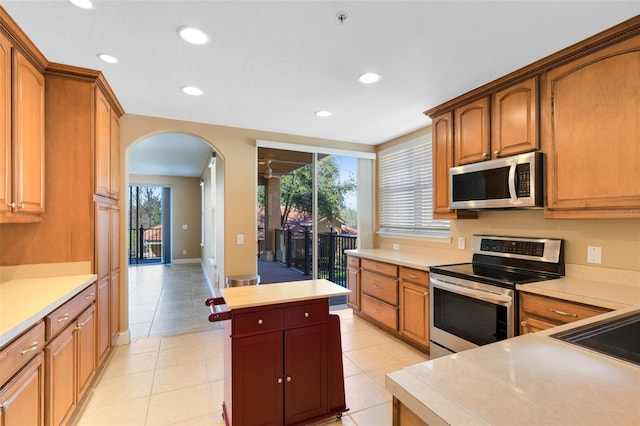 kitchen with light tile patterned floors, stainless steel appliances, a kitchen island, and a healthy amount of sunlight