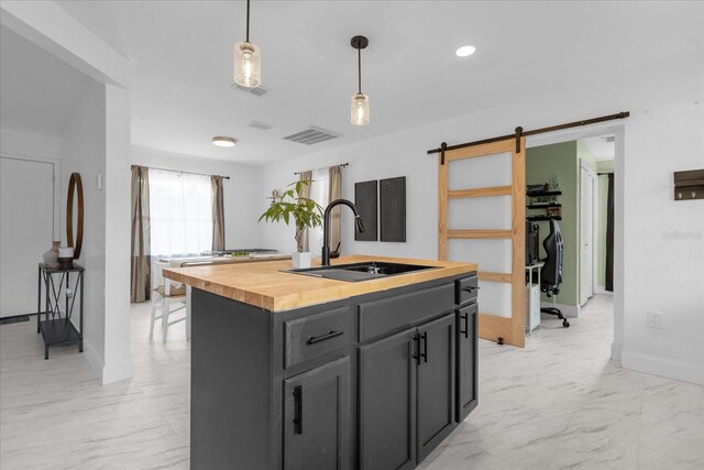 kitchen with a barn door, hanging light fixtures, a center island with sink, sink, and butcher block countertops